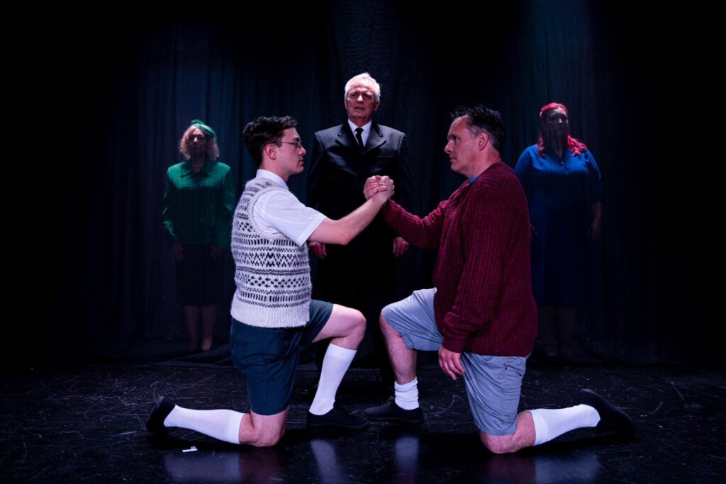 Mickey and Eddie kneel, hands clasped. Behind and between them, the Narrator is looking on. He is lit from above. Either side, the mothers stand upstage, in darkness, only just visible.