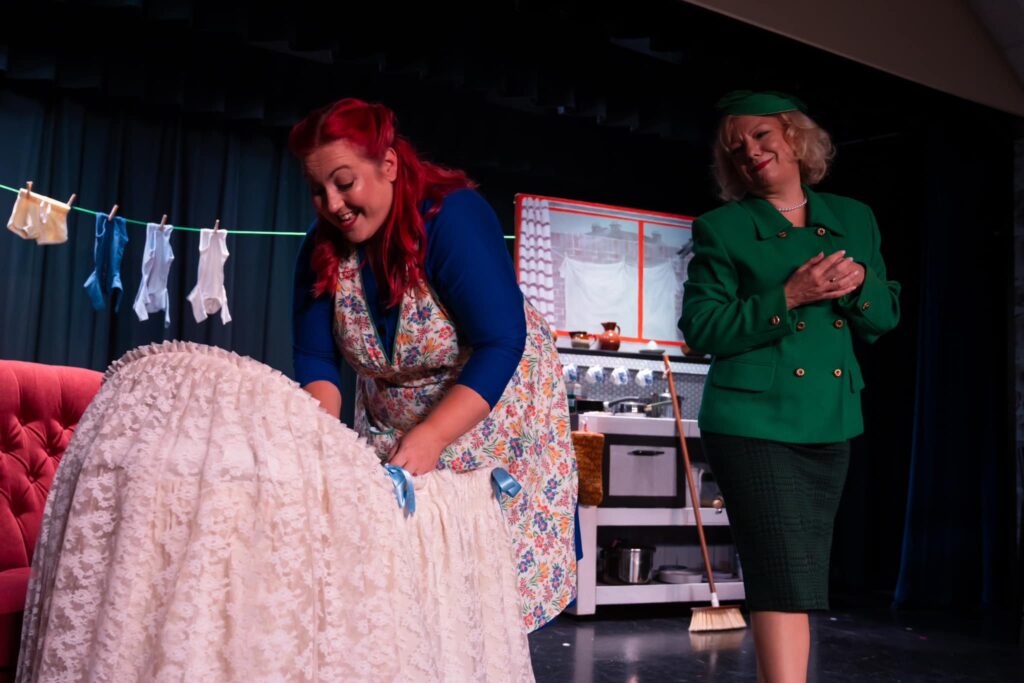 In the foreground, Mrs Johnston is leaning over a beautiful lacy bassinet. In the background, Mrs Lyons looks on.